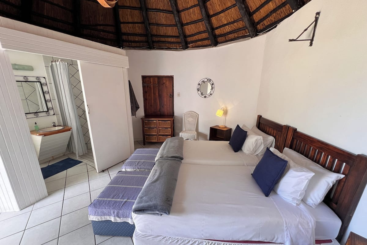 Een slaapkamer met een bed, nachtkastje, lamp en een houten garderobe.