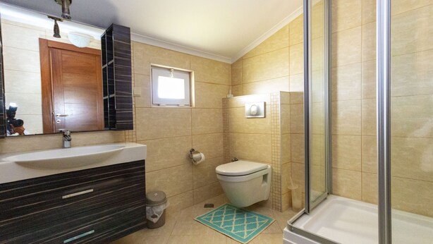 A bathroom with a wooden vanity, a toilet, a shower with a glass door, and a small window. - Paradise Town Villa Marina (Serik)