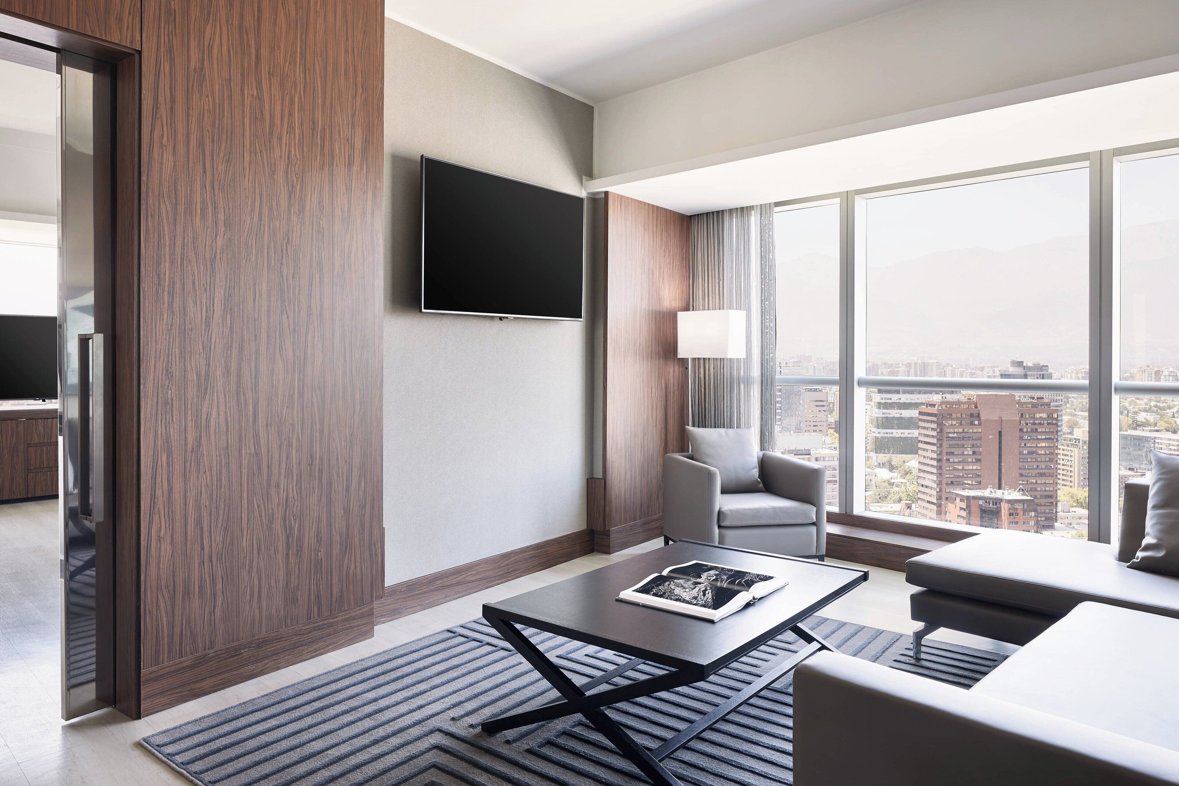Et moderne hotelværelse med et stort vindue, et fladskærms-tv, en sofa og et sofabord.