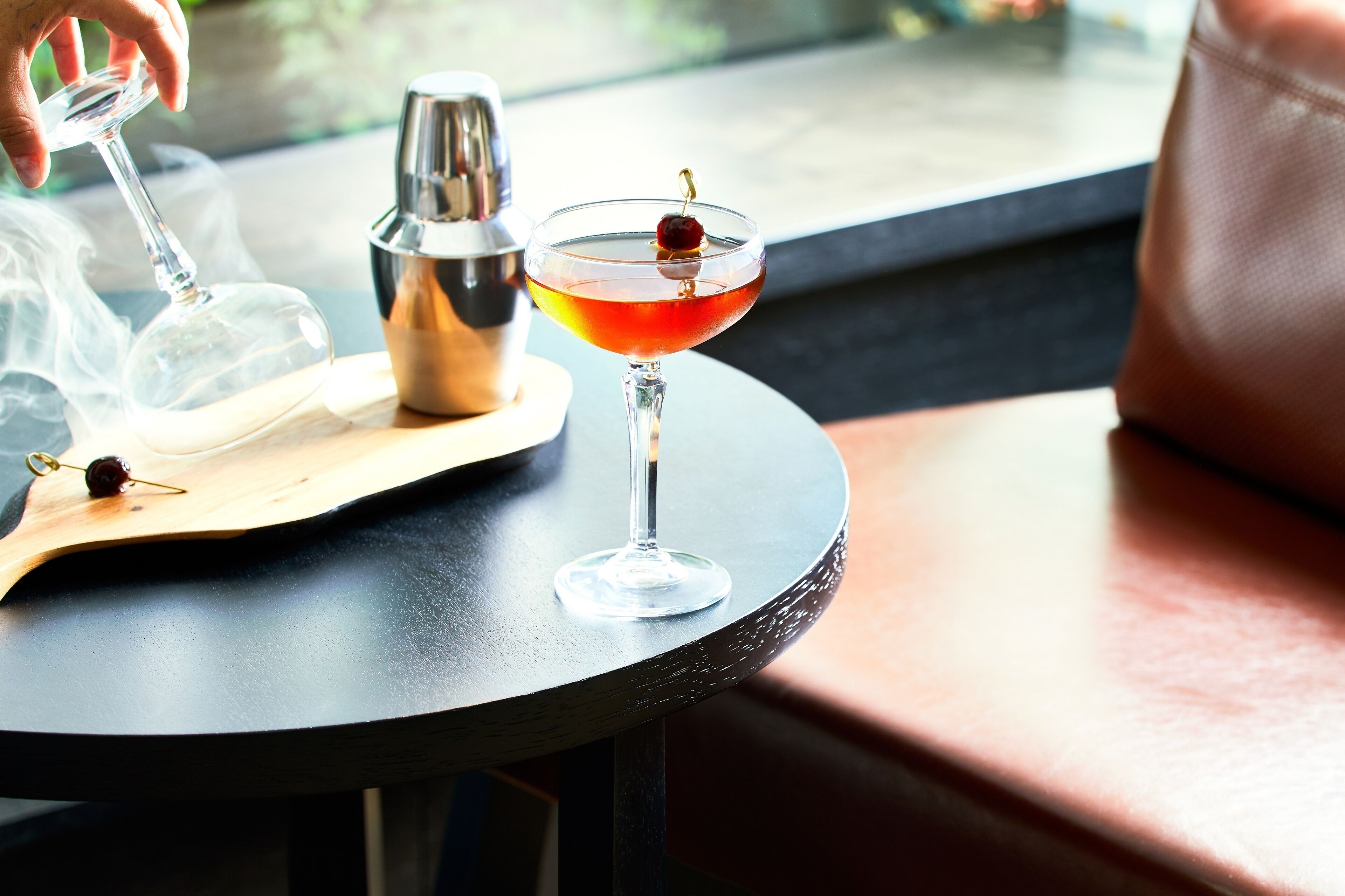 Un verre à cocktail, orné d’une cerise, posé sur une table ronde.