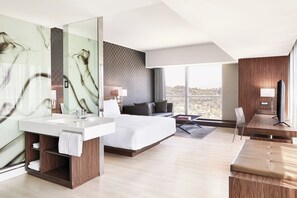 Una habitación de hotel moderna con una cama grande, una tocador con espejo, un escritorio y vistas a la ciudad.