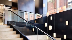 Una escalera moderna con barandillas de vidrio y un muro con patrón geométrico.