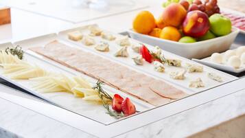 Un bufé con diversos quesos, carnes y frutas.