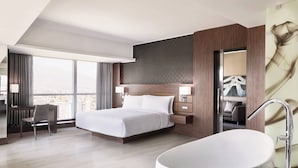 Habitación de hotel moderna con una cama grande, zona de estar, bañera y vistas a la ciudad.