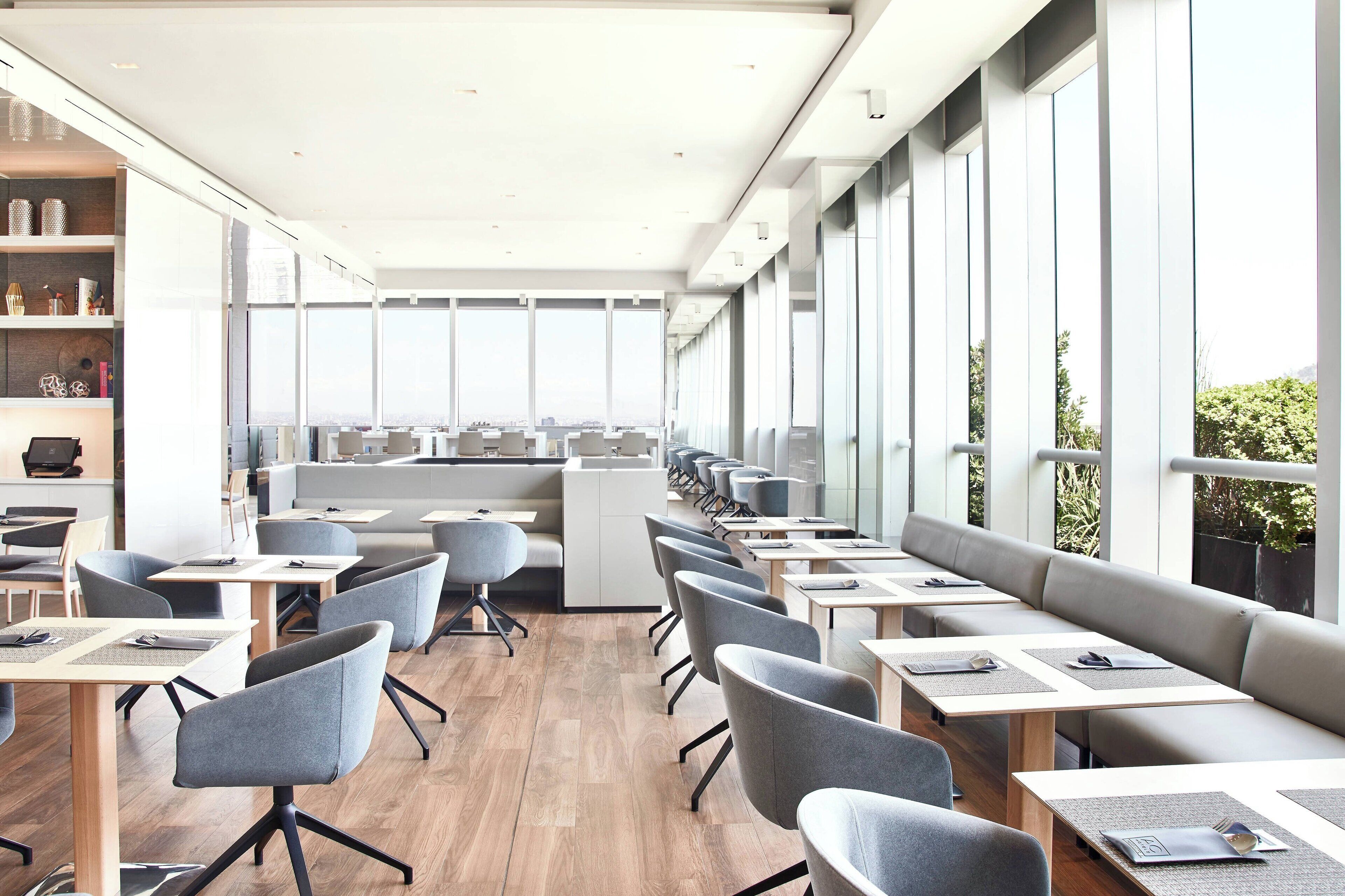 Un comedor moderno con mesas largas, sillas grises y vistas a la ciudad a través de amplios ventanales.
