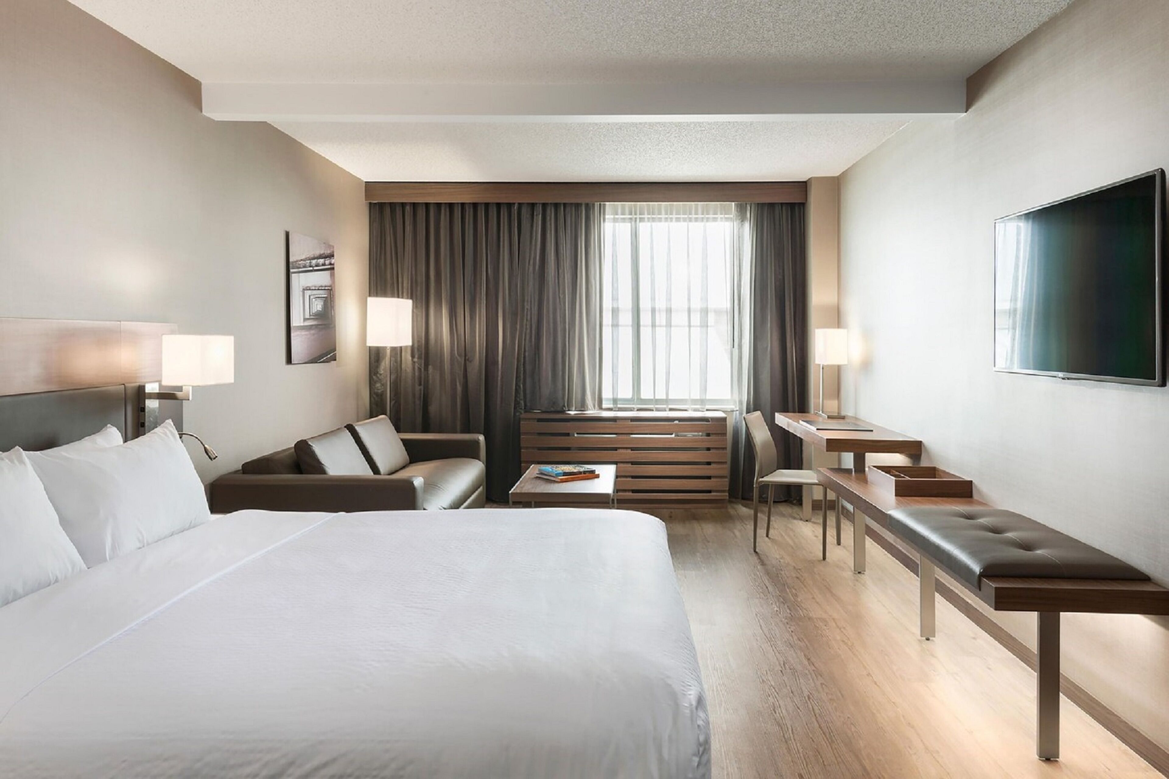 Una habitación de hotel moderna con una cama grande, un sofá, un escritorio y un televisor.
