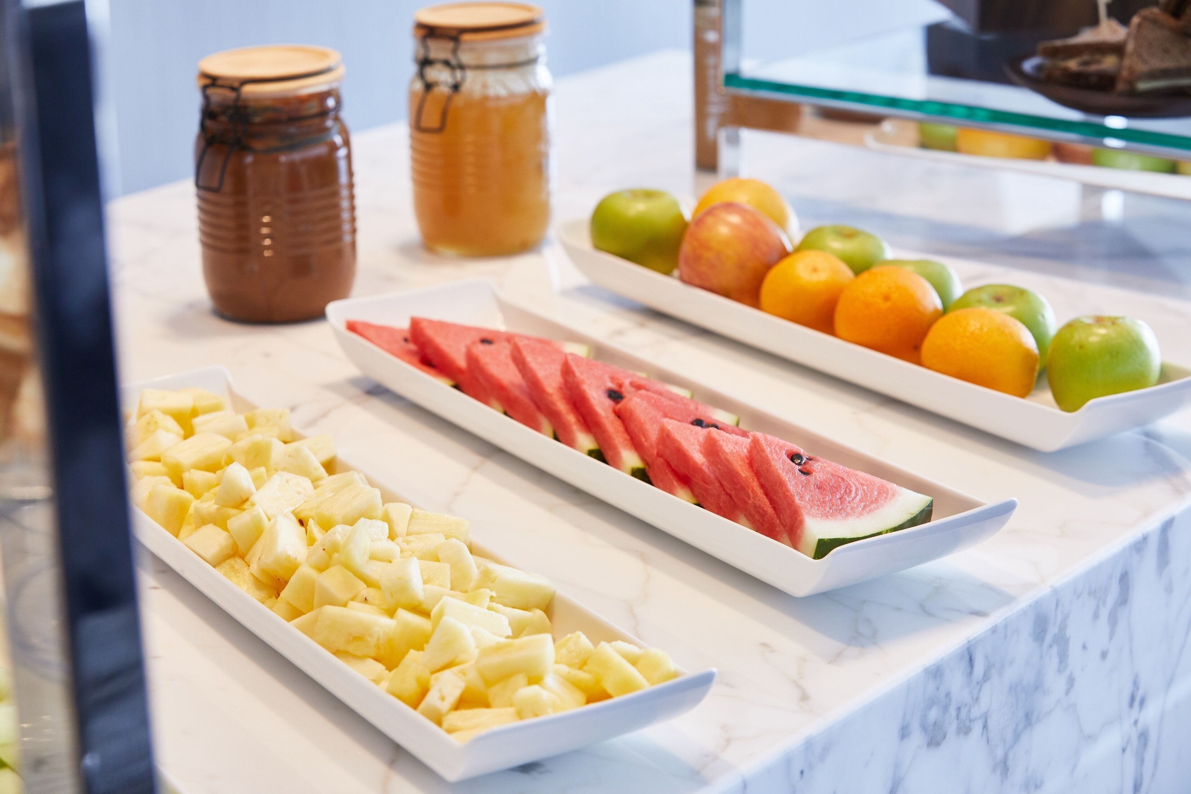 A buffet with various fruits and a jar of honey.