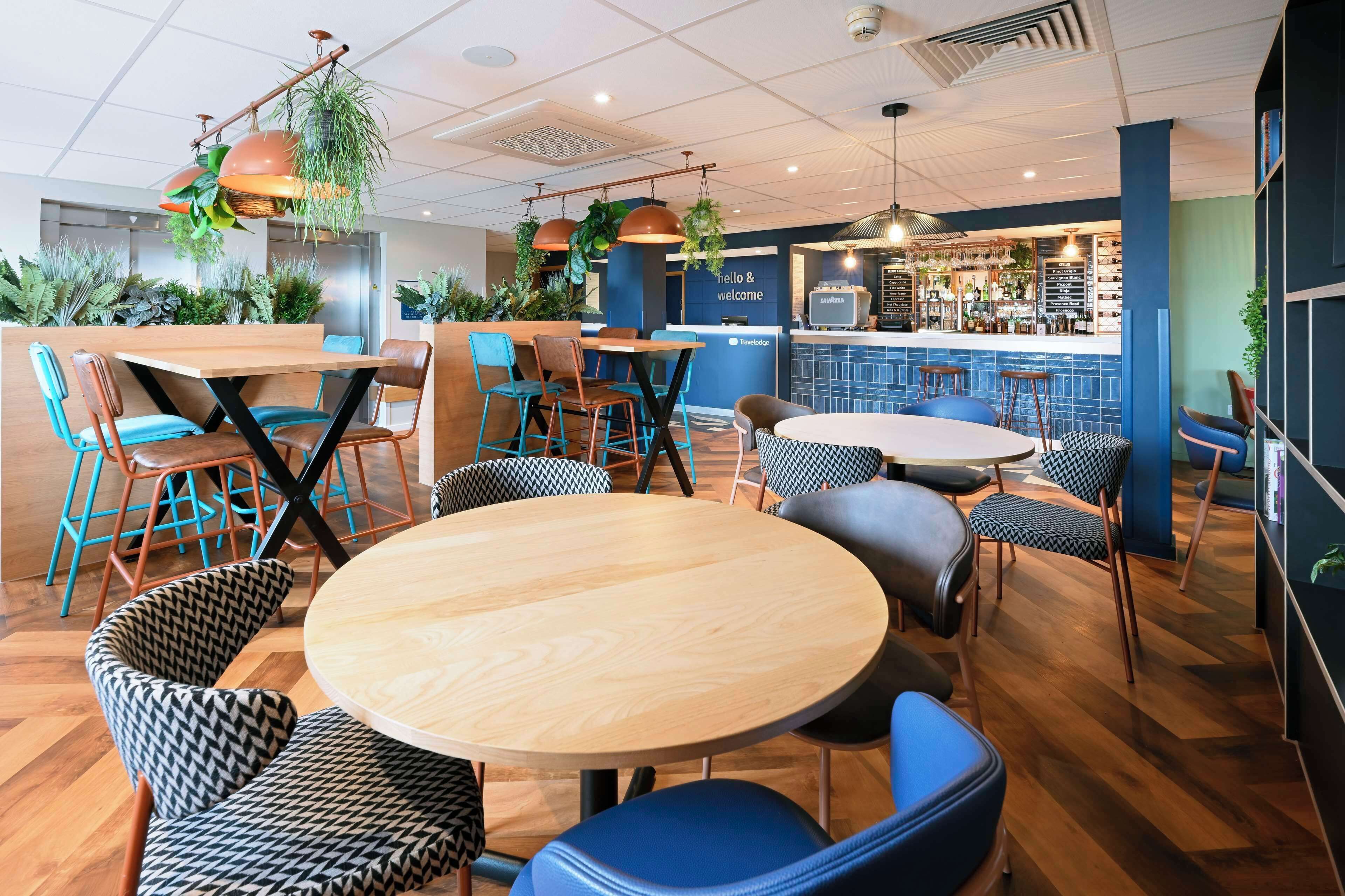 A modern cafe with round wooden tables and blue and black patterned chairs.