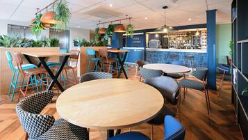 A modern cafe with round wooden tables and blue and black patterned chairs.