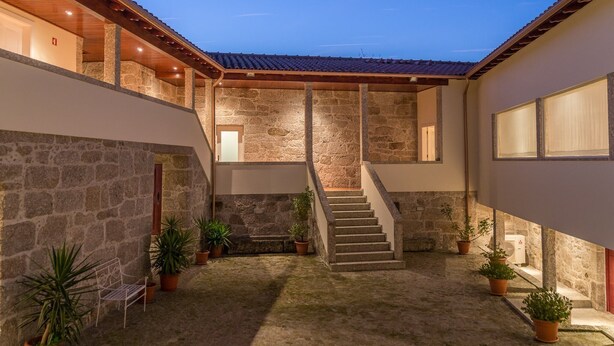 A courtyard with a stone staircase leading to an upper level, surrounded by potted plants and a bench. - Casa do Outeiro (Povoa de Lanhoso)