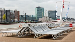Een rij ligbedden op een terras met een stadsachtergrond.