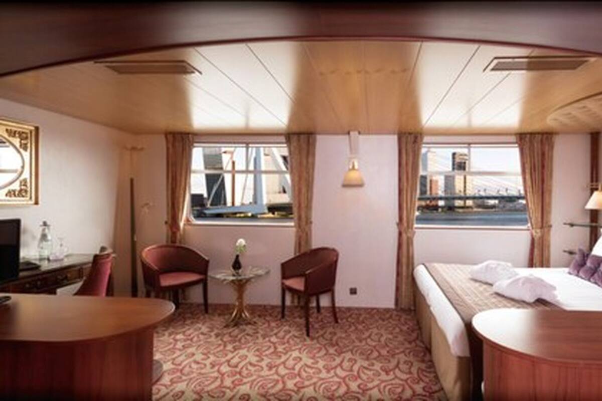 Ein Zimmer mit einem Bett, zwei Stühlen, einem kleinen Tisch, einem Schreibtisch und einem Fenster mit Blick auf eine Brücke.
