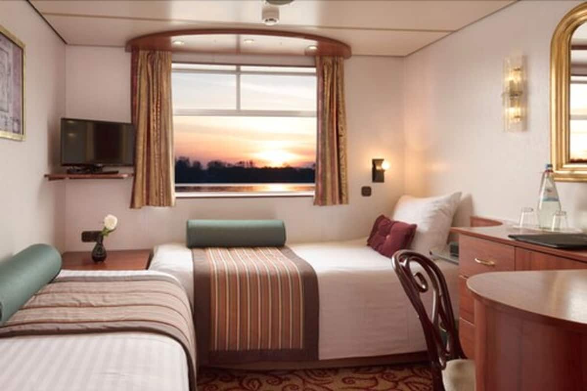 Ein Hotelzimmer mit zwei Betten, einem Fernseher, einem Schreibtisch und Blick auf den Sonnenuntergang.