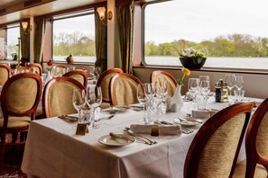A dining area with tables set for a meal, chairs, and a view of the water outside. - KNM MS Switzerland II - Frankfurt (Frankfurt)