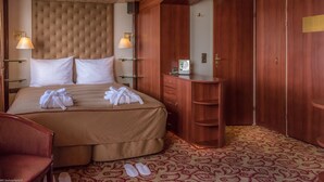 Een hotelkamer met een groot bed, een houten garderobe, een nachtkastje en een paar slippers op de vloer.