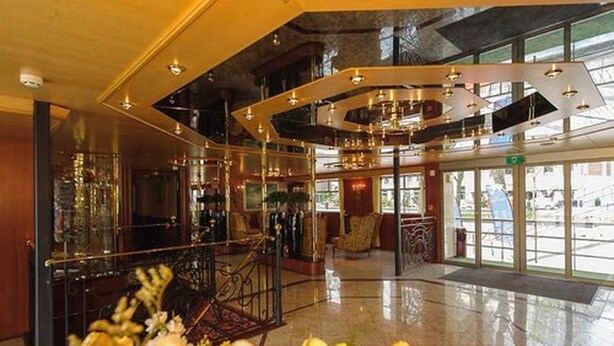 Een ruime lobby met een hoge plafond, een centrale trap en uitzicht op de straat door grote ramen.