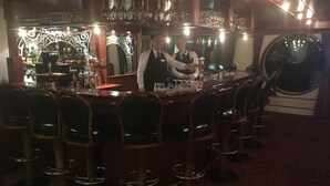 Een bar met een bartender, barstoelen en een wijnrek op de achtergrond.