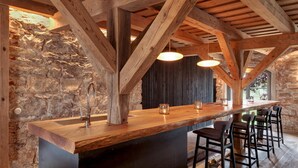 A rustic kitchen with exposed wooden beams, a stone wall, and a bar area with stools.