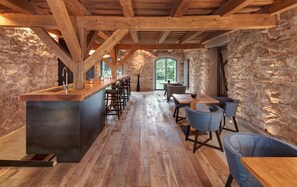 A rustic interior with a stone wall, wooden beams, a bar area, and a dining space with chairs and tables. - Landhotel AlmRefugio (Neumarkt in der Oberpfalz)