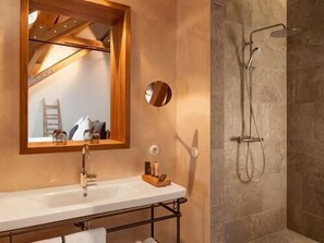 A bathroom with a wooden-framed mirror, a white sink, and a shower with a handheld showerhead. - Landhotel AlmRefugio (Neumarkt in der Oberpfalz)