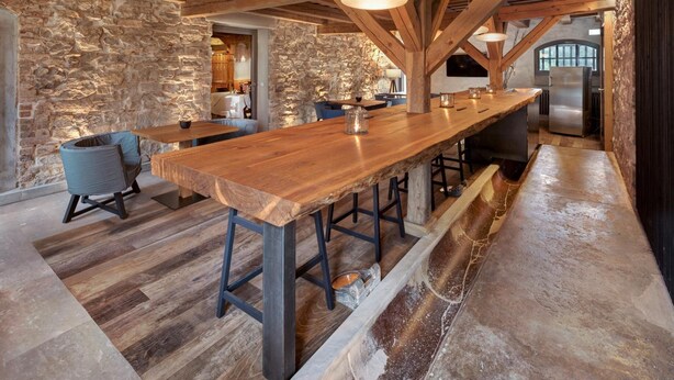 A rustic kitchen with a long wooden bar, stone walls, and exposed wooden beams.