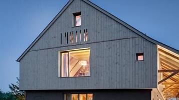 Un bâtiment moderne de style grange, doté d’un toit en pente, de grandes fenêtres et d’un espace intérieur ouvert.