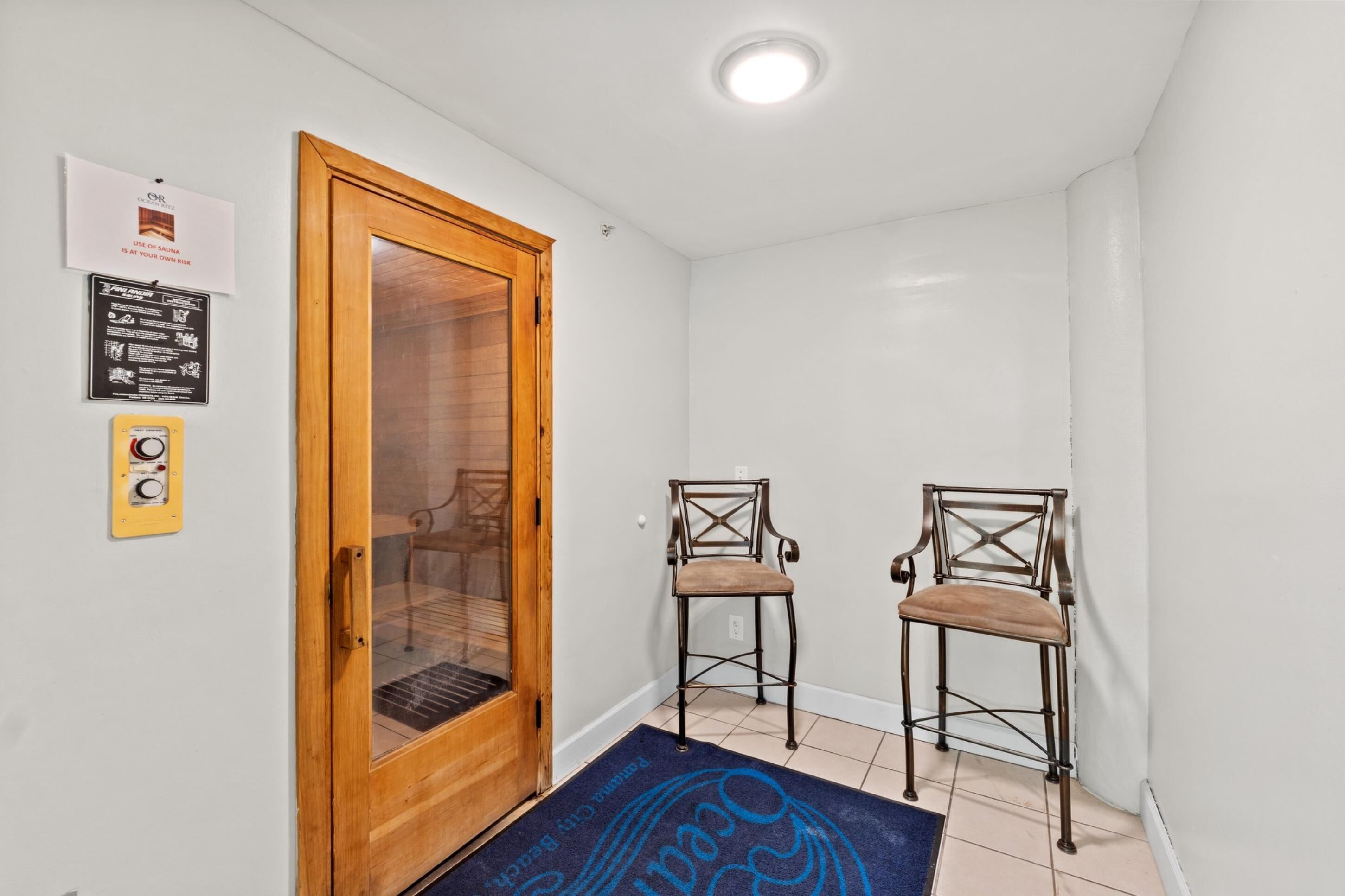 A hallway with a wooden door, two chairs, a blue mat, and a ceiling light.
