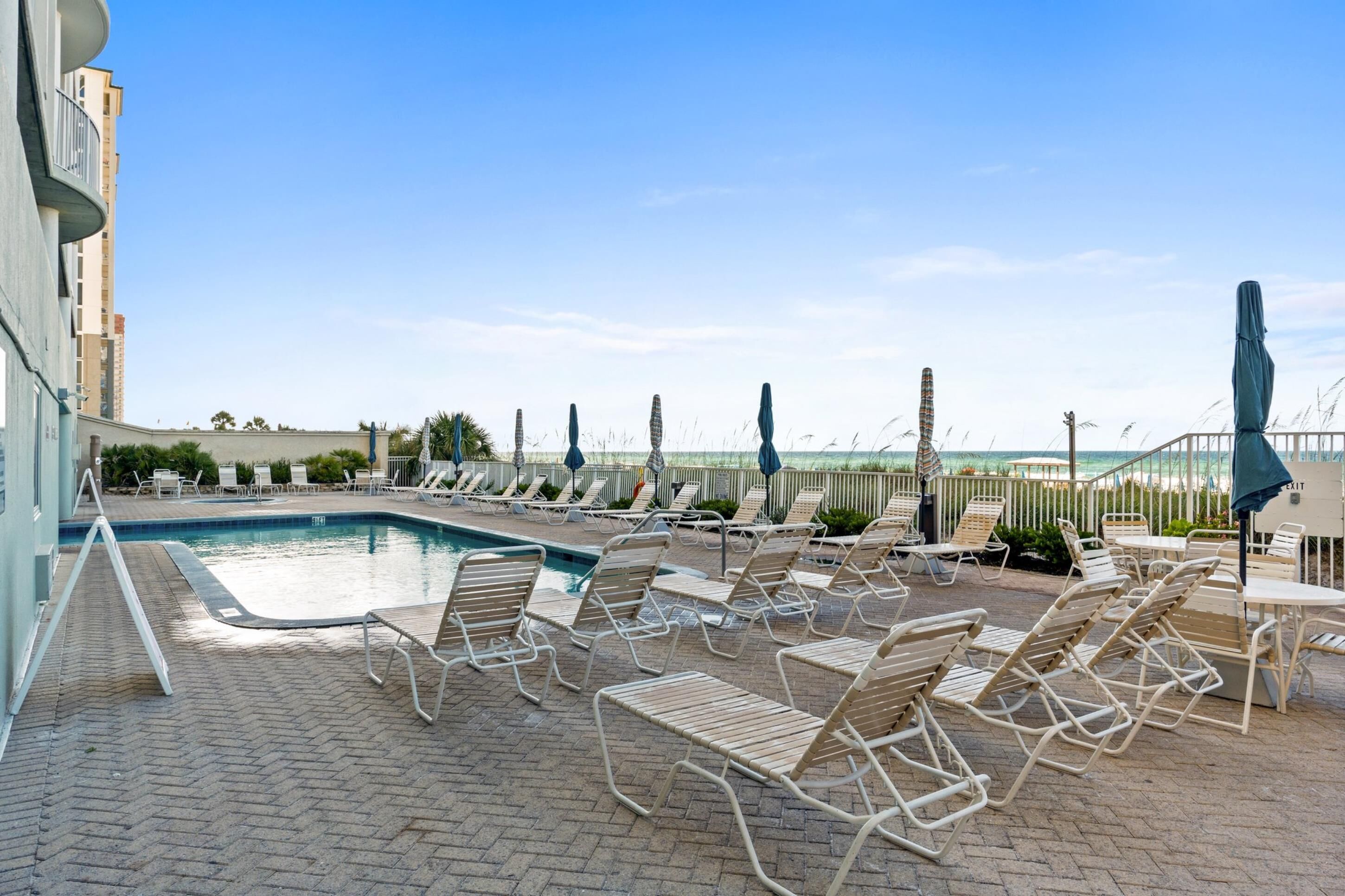 A poolside area with lounge chairs and umbrellas, overlooking a beach.