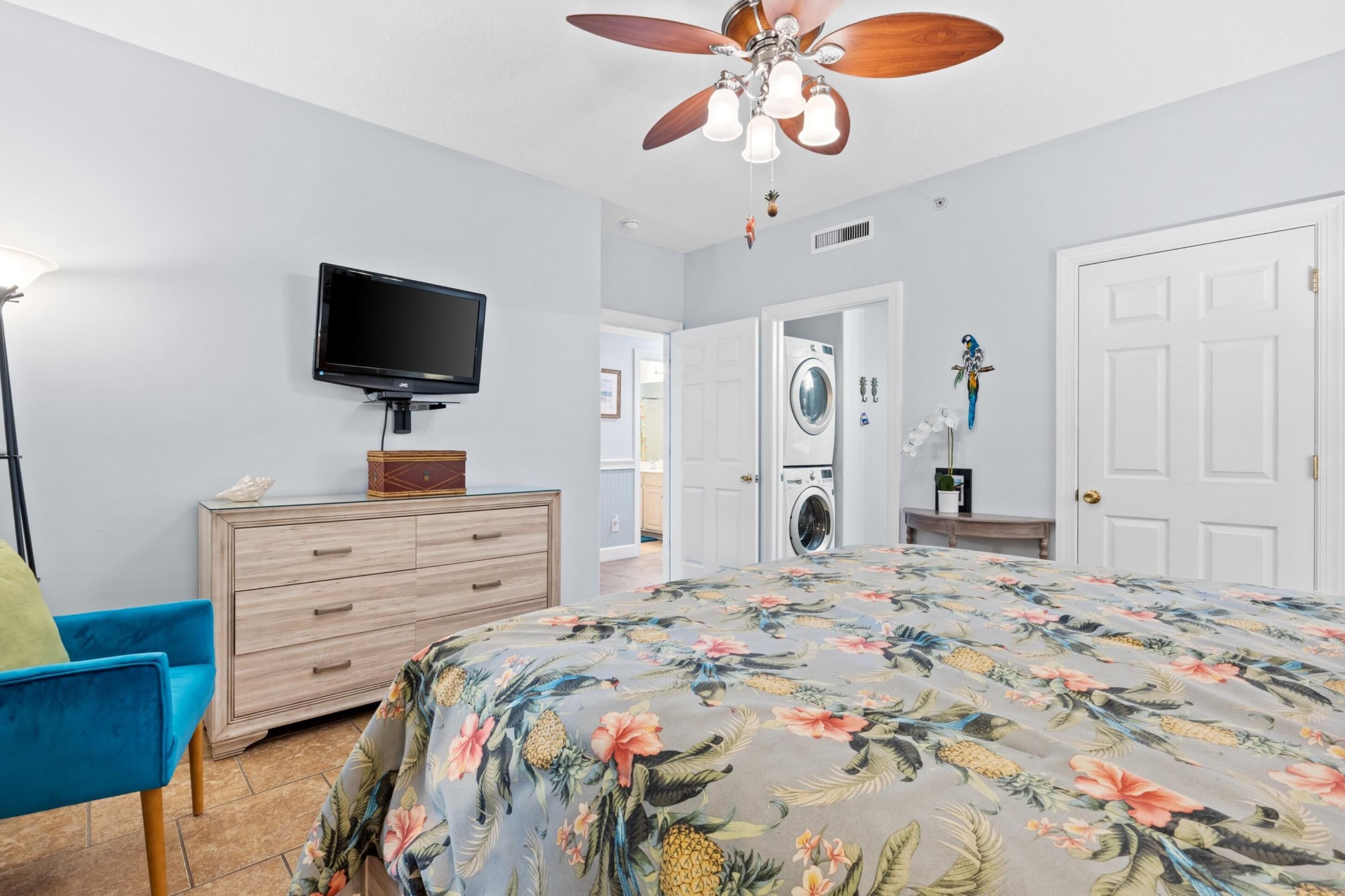 A bedroom with a bed, a television on a dresser, a ceiling fan, and a washing machine.