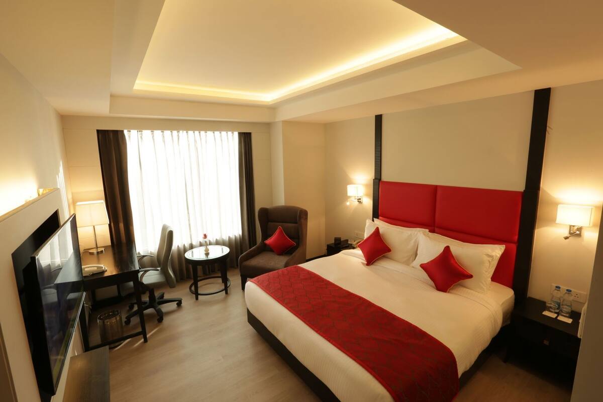 A hotel room with a large bed, a desk with a chair, a small round table, and a window with curtains.