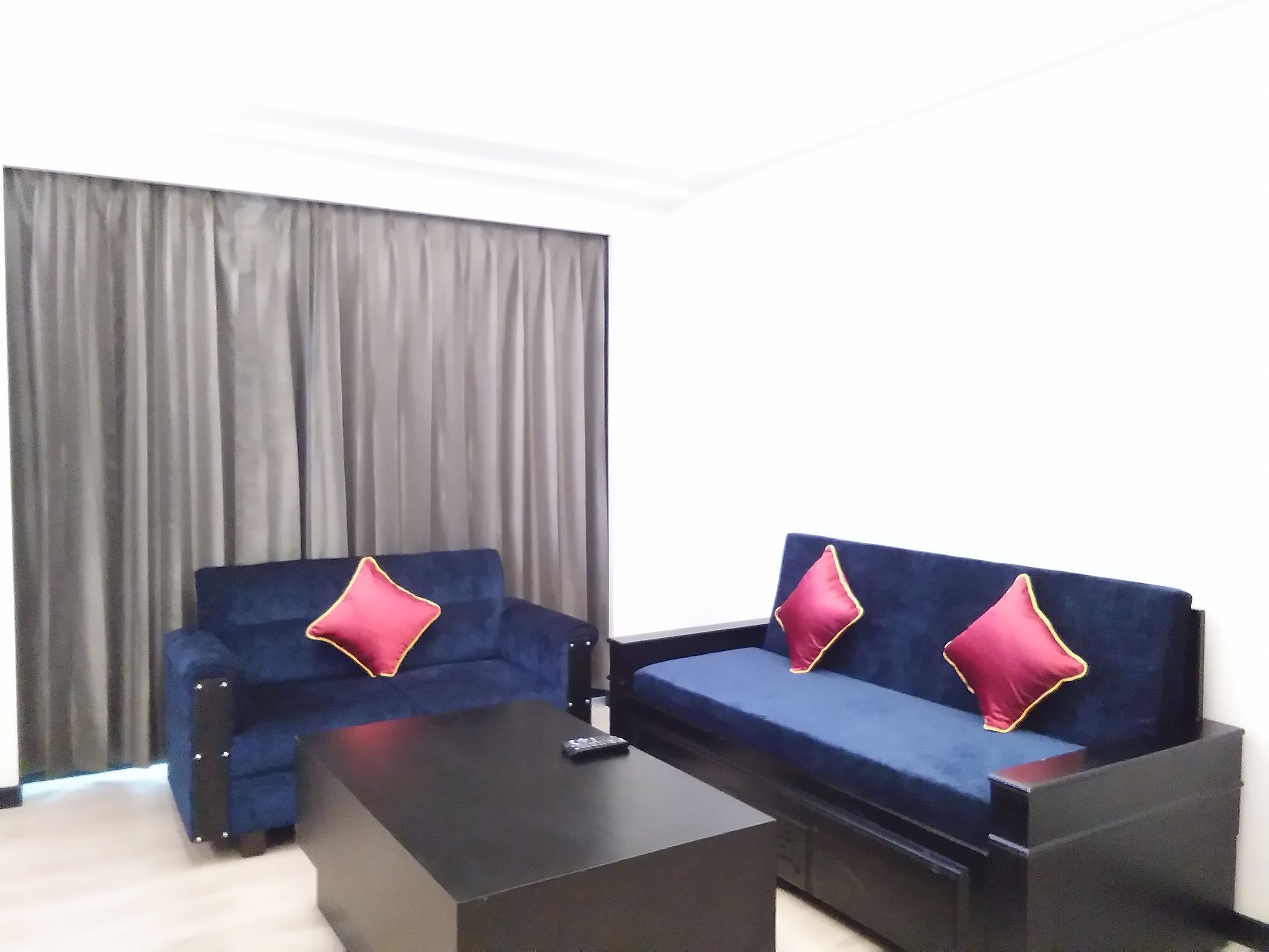 A modern living room with two blue sofas, each with a red pillow, and a black coffee table.