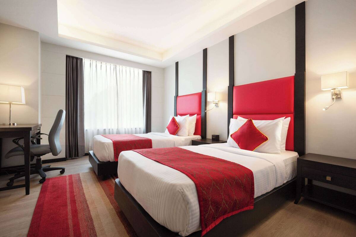 A hotel room with two beds, a desk, and a chair.