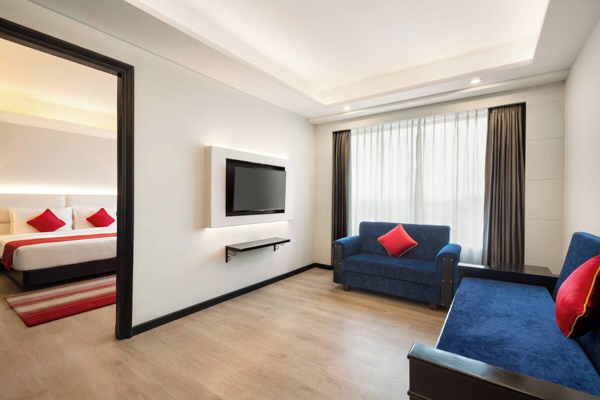 A hotel room with a bed, a sofa, a TV, and a large window with curtains.