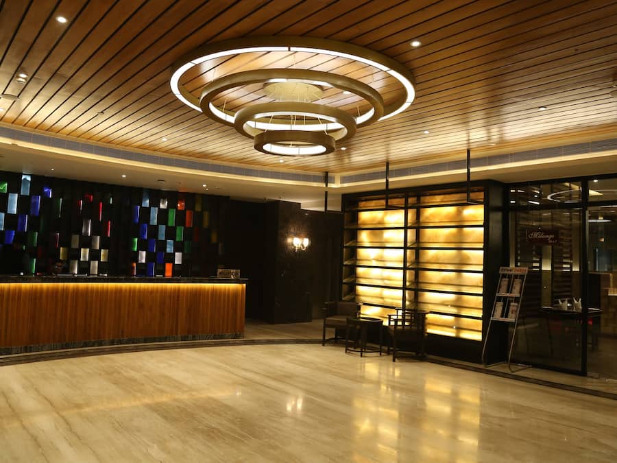 A modern hotel lobby with a wooden reception desk, a colorful wall, and a circular light fixture.