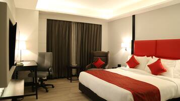 A hotel room with a large bed, a desk, a chair, and a small table.