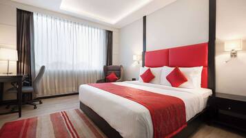 A hotel room with a large bed, a desk, and a chair.