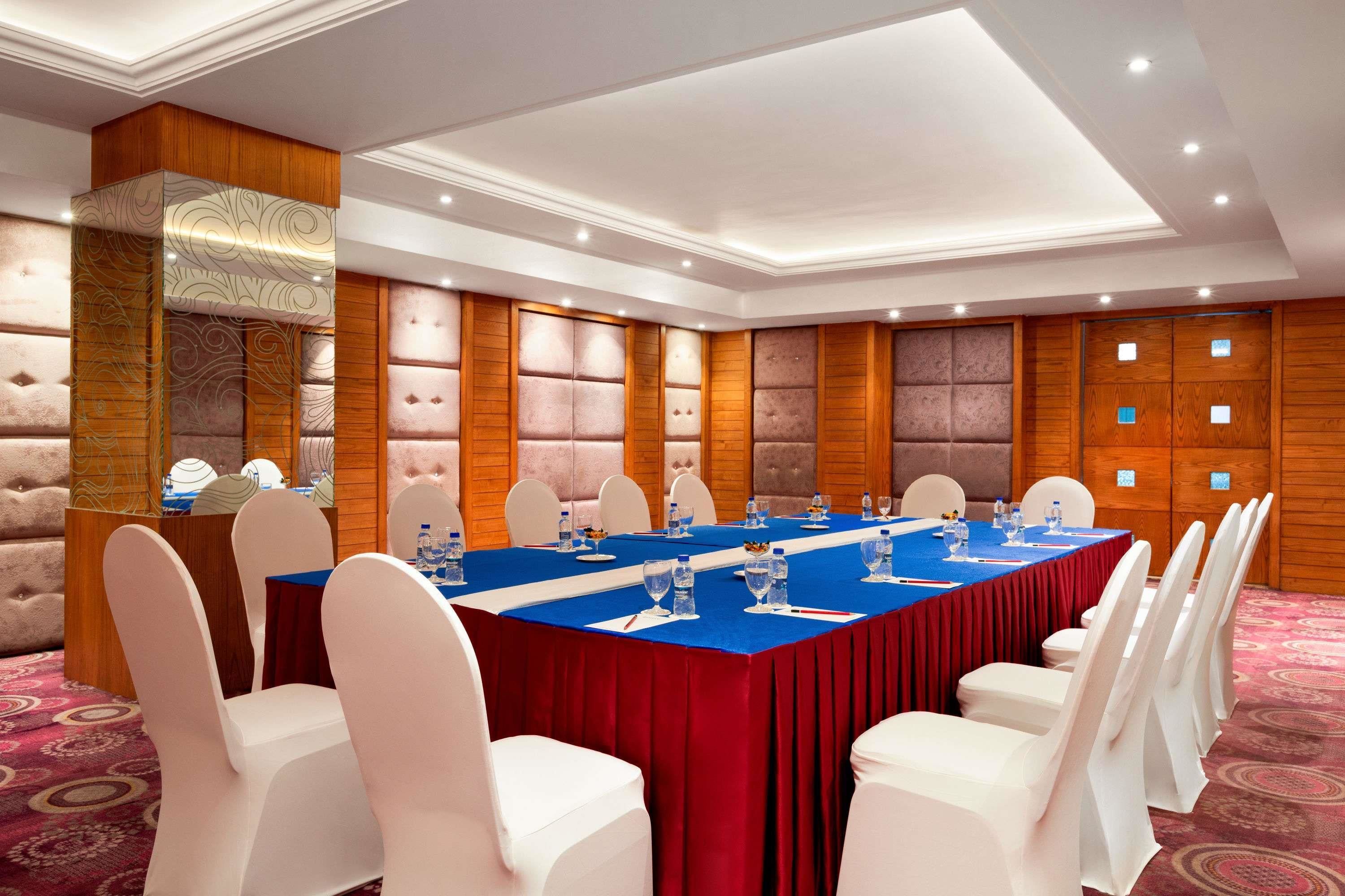Un salón de conferencias con una larga mesa, sillas blancas y un mantel rojo.