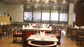 A restaurant interior with multiple dining tables and chairs, a central island, and a large window with a view of the street.