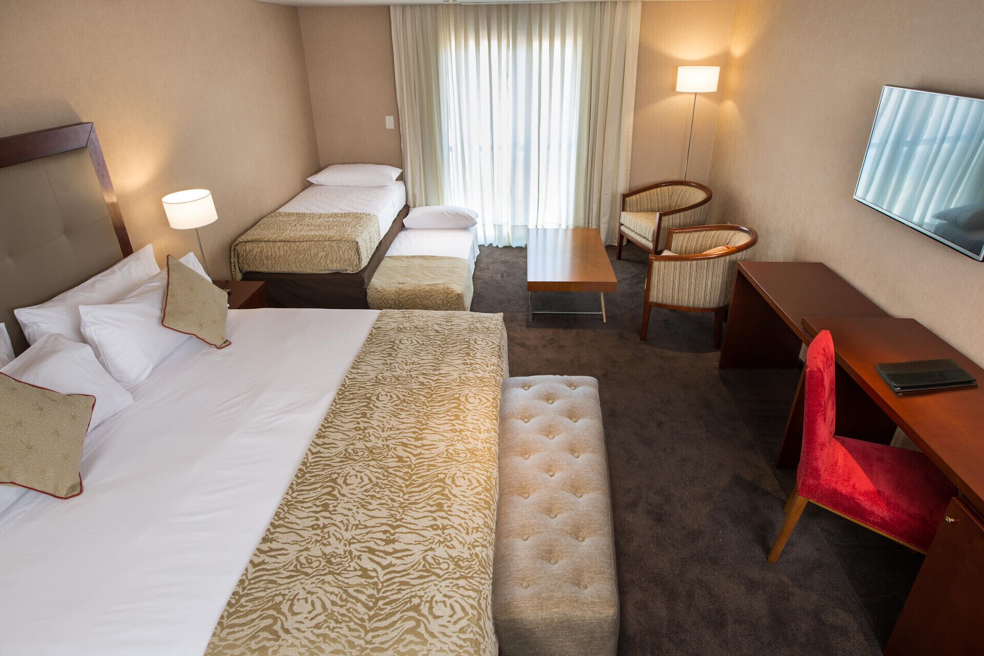 Une chambre d’hôtel avec un grand lit, deux petits lits, un bureau, une chaise, un canapé et un téléviseur.