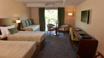 A hotel room with two beds, a desk, a chair, and a small table with a vase.