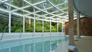 An indoor swimming pool with glass walls, a stone wall, and a tiled floor.