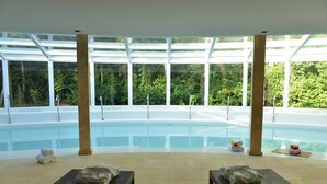 A poolside area with two lounge chairs, a glass-enclosed pool, and a view of lush greenery.