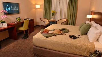 A hotel room with a bed, desk, chairs, and a television displaying the hotel's name.
