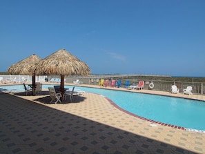 Área de piscina com espreguiçadeiras e um guarda-sol de palha, com vista para o mar.