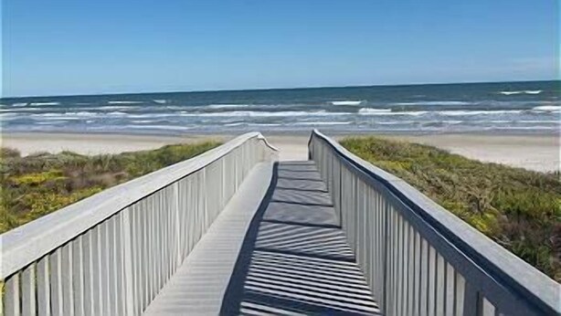 Une promenade en bois qui mène à une plage, avec des vagues en arrière-plan.
