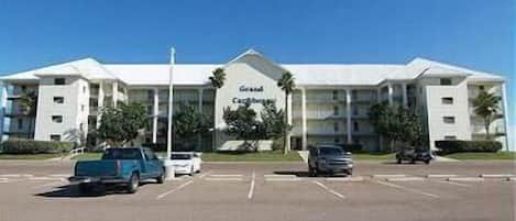 A hotel with a central entrance, multiple floors, and a parking lot with several cars.