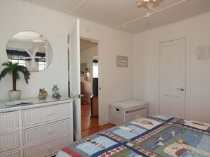 A bedroom with a bed, a dresser, a mirror, a door, and a small white basket.