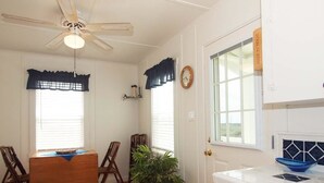 Una habitación con una mesa de comedor, sillas, un ventilador de techo, una planta en maceta y una zona de cocina con un fregadero y encimera.