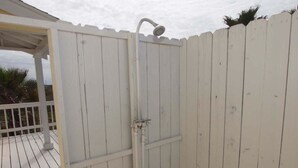 Un portón blanco de madera con una ducha, una cerca blanca y una terraza de madera.