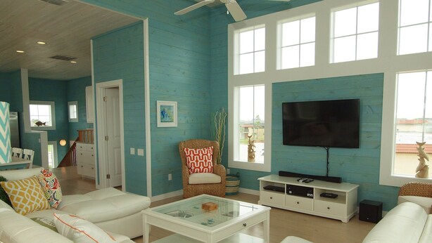 A spacious living room with a large TV, white sofas, and a ceiling fan.